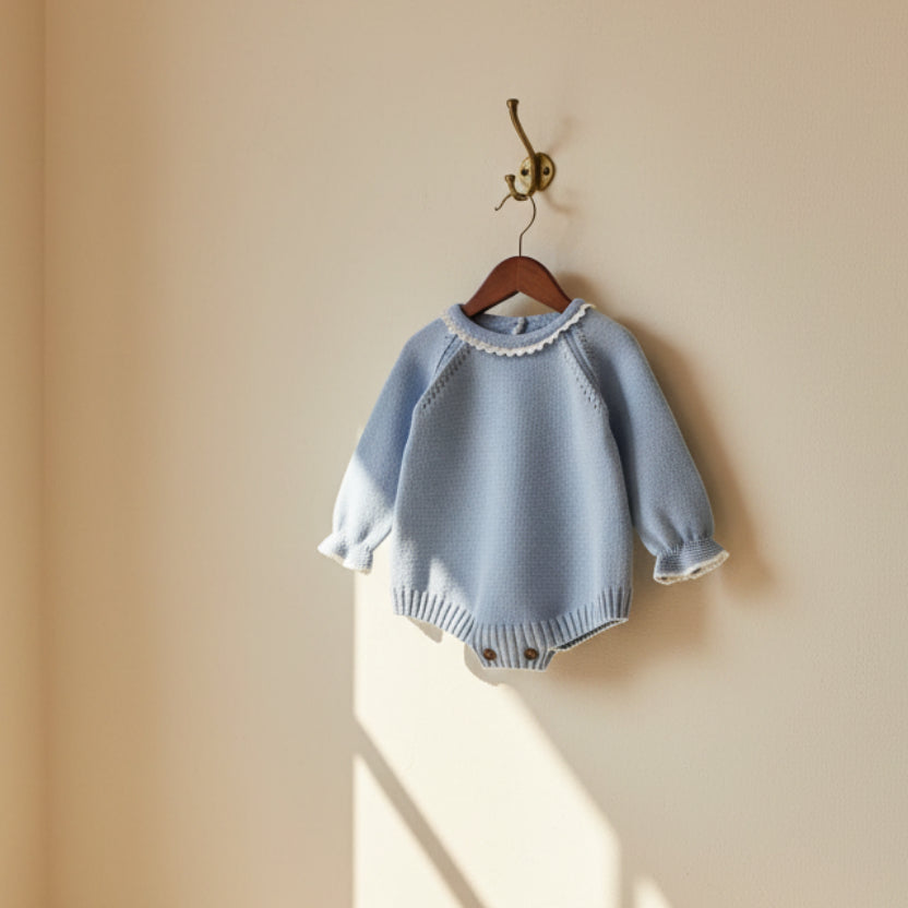 Baby blue knitted romper displayed on wooden hanger showing front design