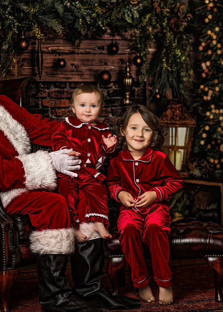 Two children wearing coordinating red velvet Christmas nightwear beside Santa.