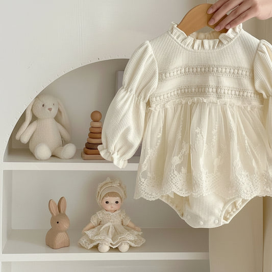 Oh Delilah Cream long-sleeved baby romper with intricate floral lace tulle overlay hanging on a wooden hanger on a nursery shelf