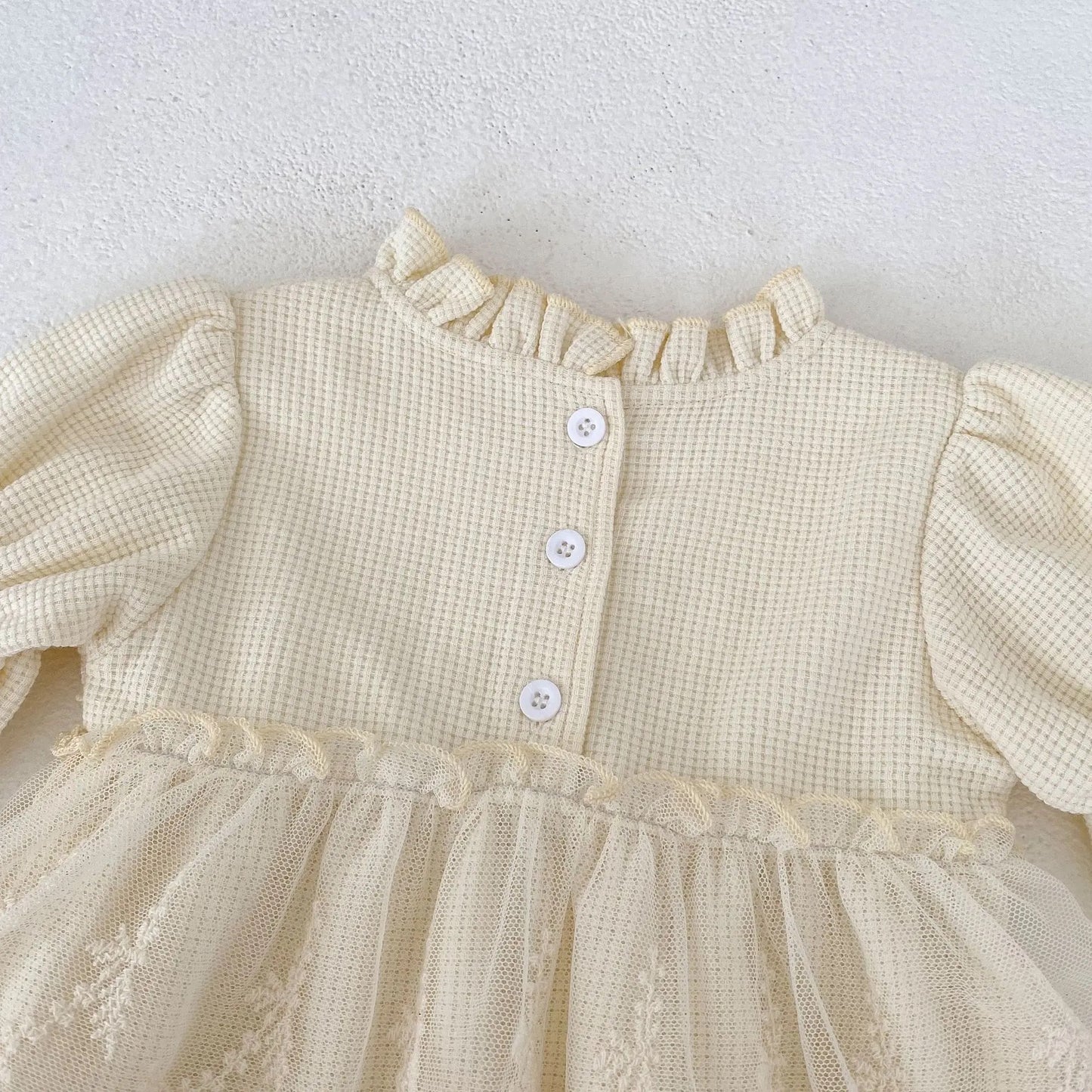A close-up of a cream Oh Delilah Romper back detail with button fastening and ruffled neckline from Little Babybox