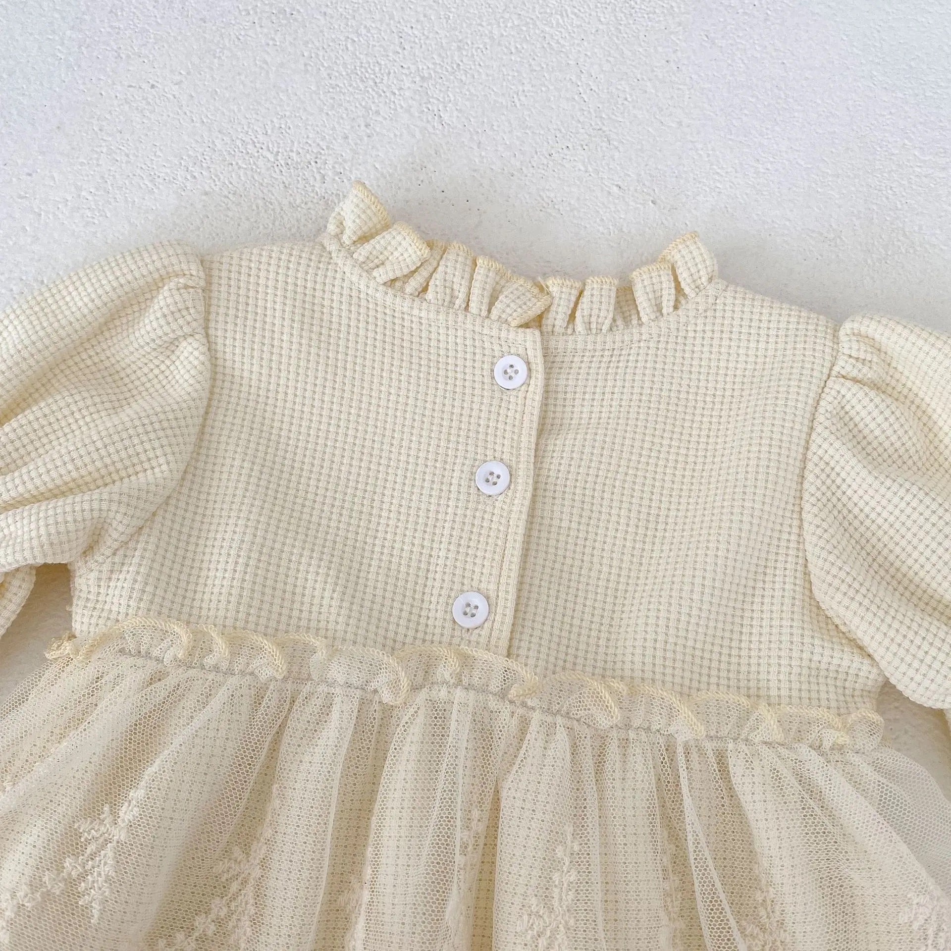 A close-up of a cream Oh Delilah Romper back detail with button fastening and ruffled neckline from Little Babybox