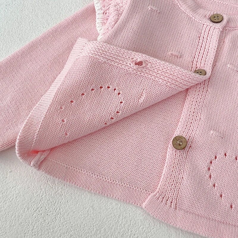 Close-up of Paloma pale pink knit cardigan showing wooden button fastening and openwork heart stitch detail - Little Babybox