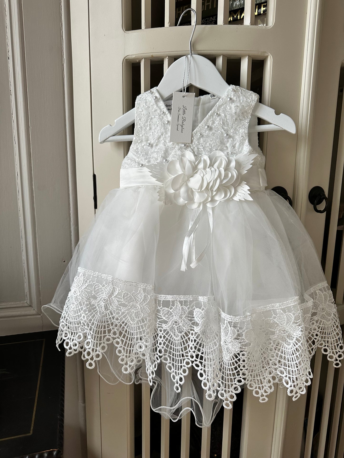 Detailed view of the handmade fabric flower centerpiece and embellished V-neck bodice on the ivory white special occasion baby dress by Little Babybox