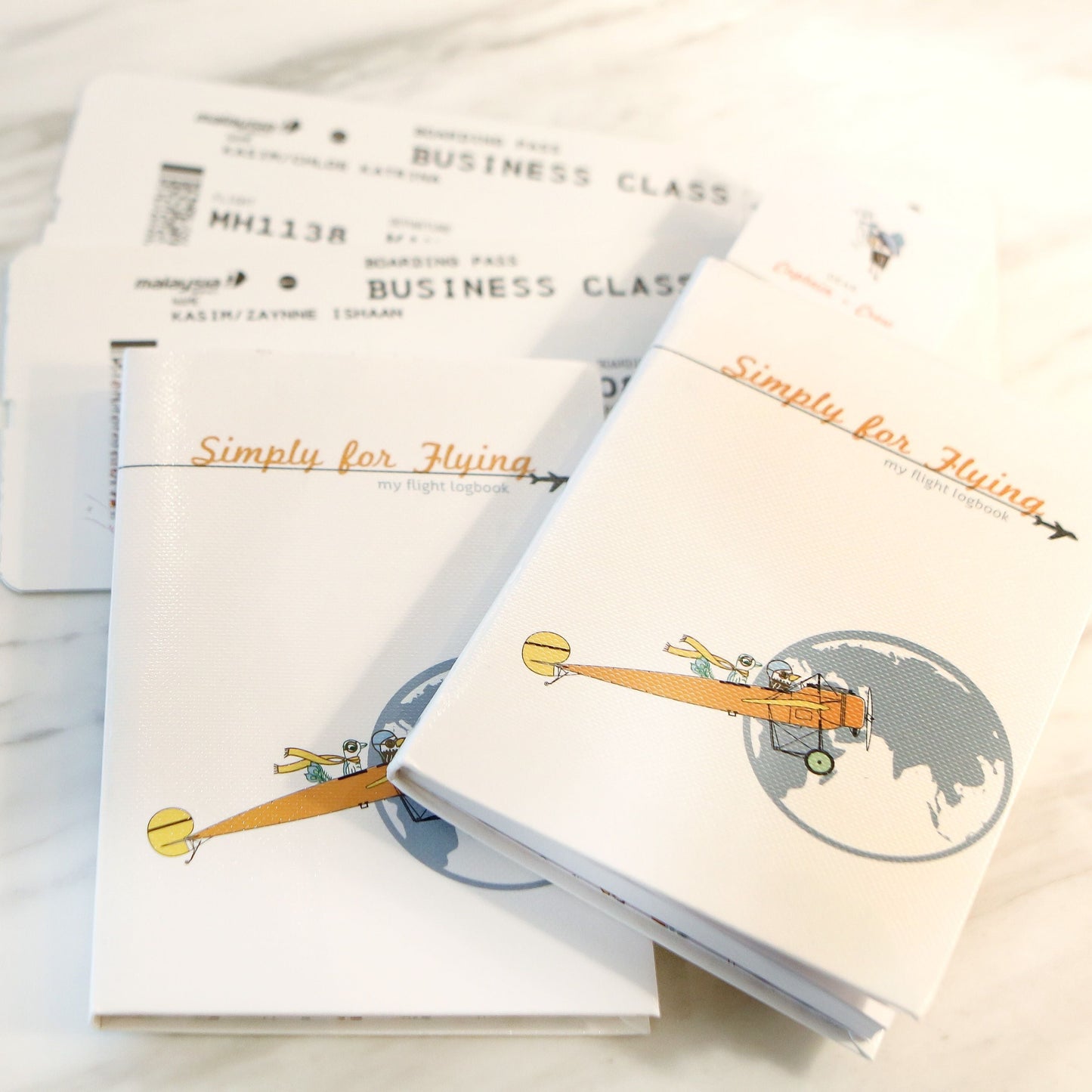 Two Simply for Flying logbooks with airline tickets on a marble surface