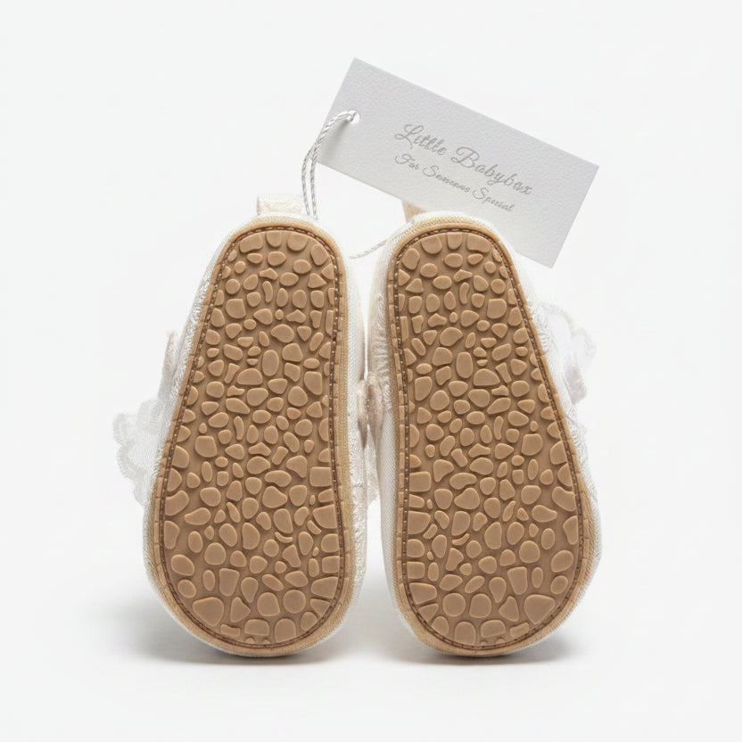 Bottom view of Aurelia fabric baby shoes displaying a pair of tan textured non-slip rubber soles with a brand tag