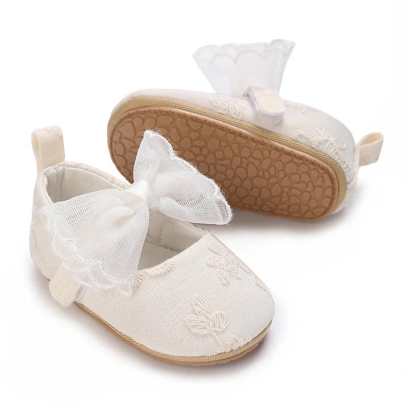 Three-quarter view of the Aurelia white fabric baby shoes displaying the delicate embroidered pattern and a tilted textured non-slip sole