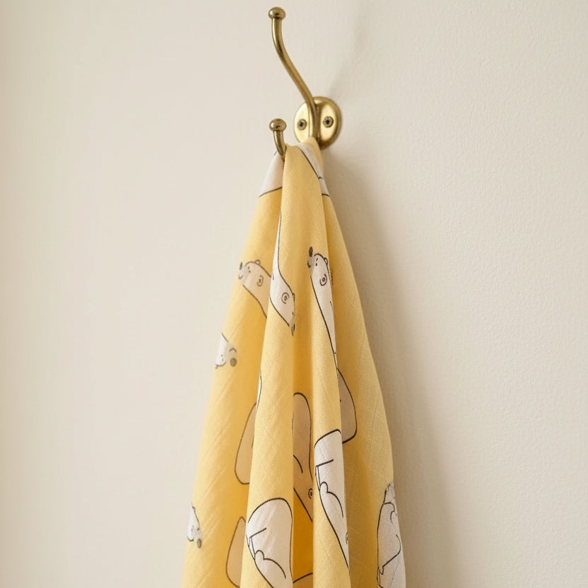 Premium mustard yellow polar bear patterned muslin swaddle blanket hanging from an elegant brass wall hook by Little Babybox